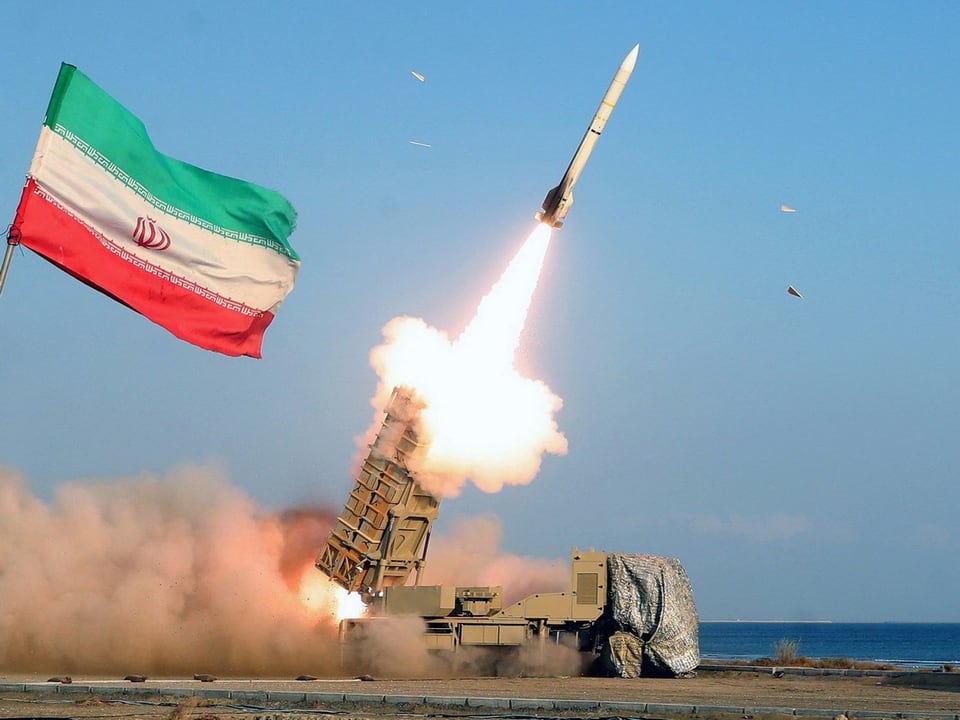Eine Rakete steigt aus einer Batterie auf. Am Bildrand ist eine iranische Flagge zu sehen.