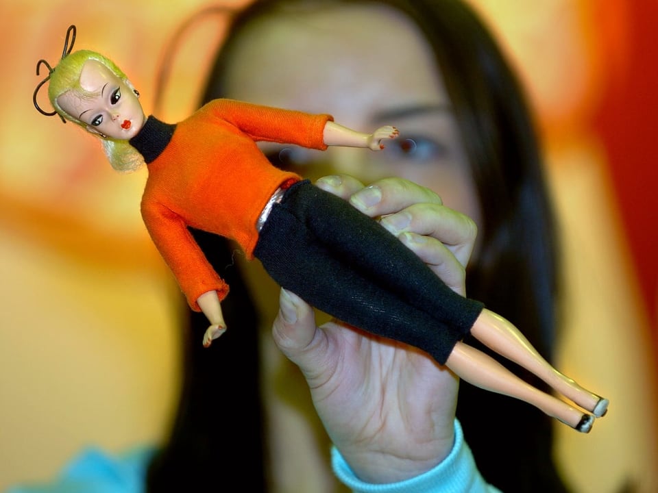 Barbie mit rotem Pulli und schwarzem Rock in der Hand einer Frau.