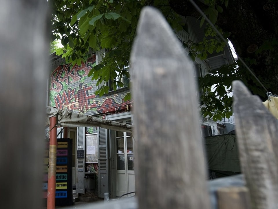 Im Vodergrund ist ein Zaun und im Hintergrund die Anlaufstelle des Contacts mit Graffitis an den Wänden.