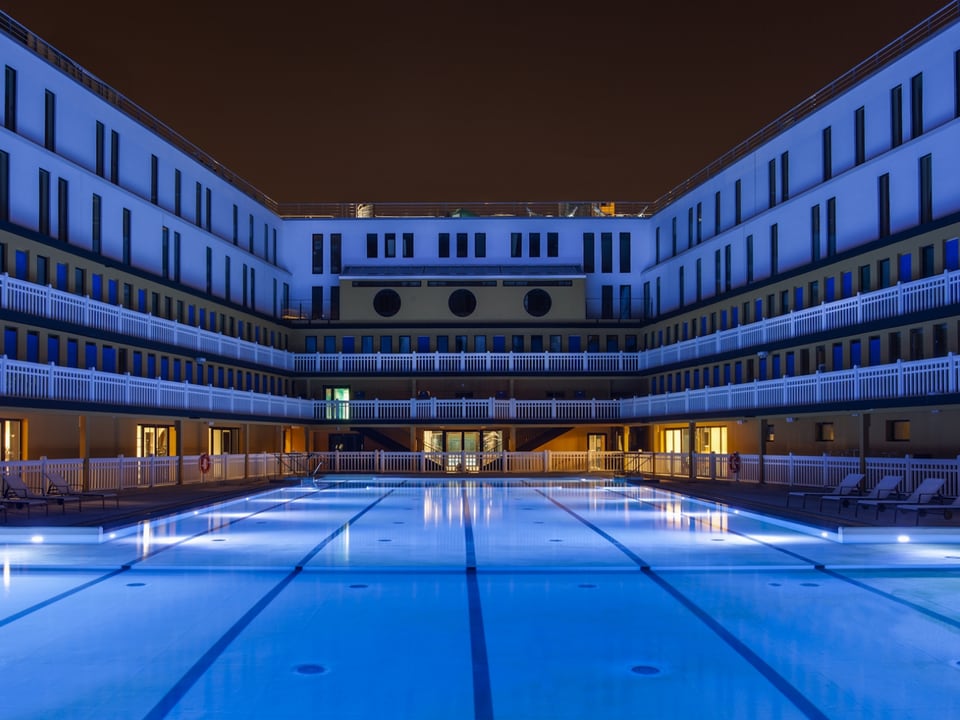 Schwimmbecken, umgeben vom Garderobengebäude bei Nacht. 