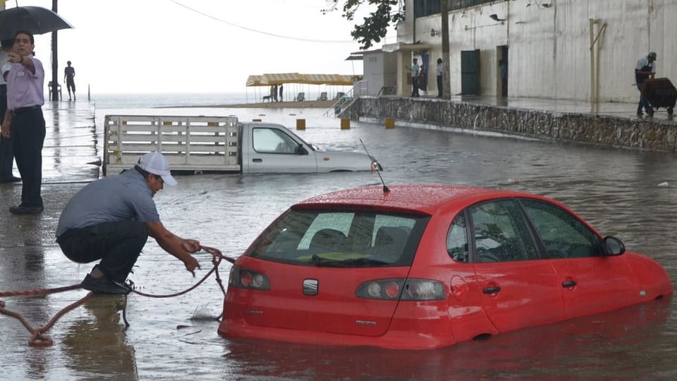 Ein Mann versucht ein Sicherungsseil an einem Auto im Wasser anzubringen.