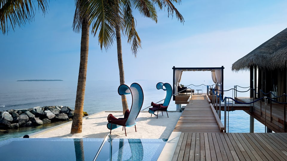 Ein Pool mit futuristische Liegestühlen und einem Bungalow mit Sicht aufs Meer.