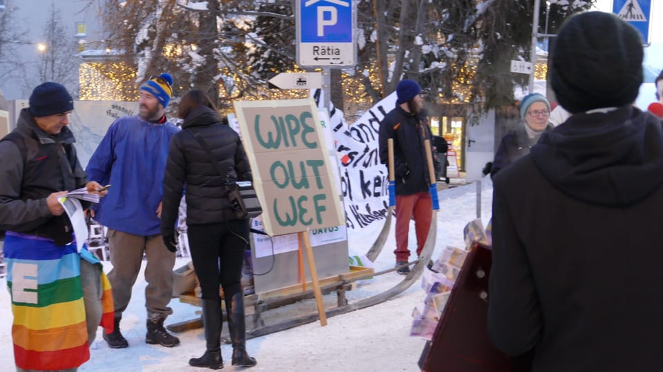 Ein paar Personen stehen rund um ein Plakat mit der Aufschrift "Wipe Out WEF".