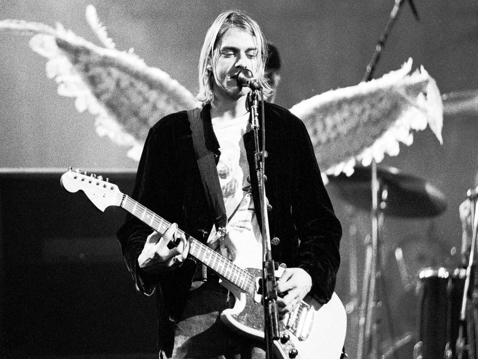 Kurt Cobain mit Gitarre auf der Bühne. Das Bühnenbild lässt es so aussehen, als ob er Engelsflügel hätte.