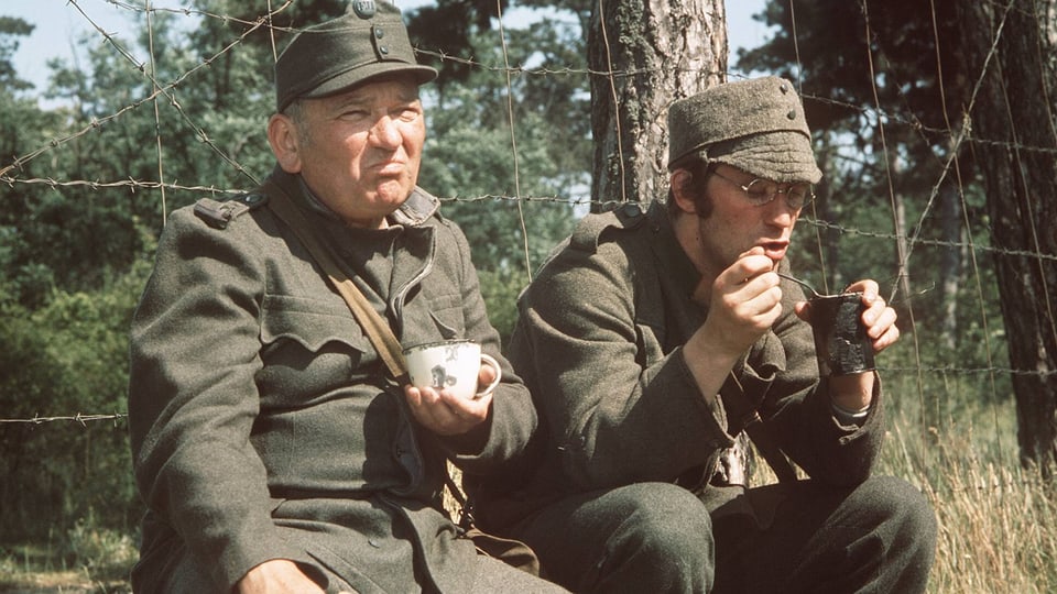 Zwei Soldaten sitzen an einem Zaun und trinken Kaffee