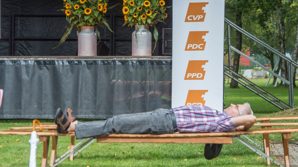 Eine Person ruht sich auf einer Festbank vor einem CVP-Logo aus.