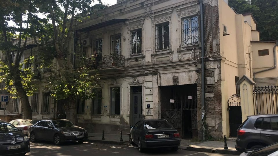 Eine verwittertes Haus in Tiflis, vor dem teure Autos parken.