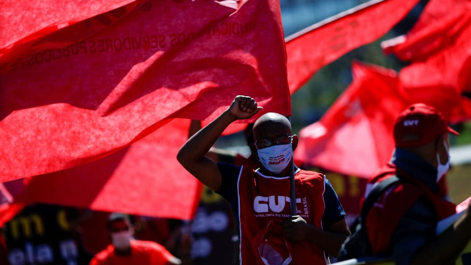 Demonstrierende in roten Shirts vor einer roten Fahne.