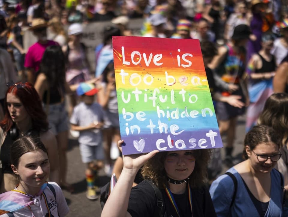 Eine Person hält ein Schild in die Luft mit der Aufschrift «Love is too beautiful to be hidden in the closet»