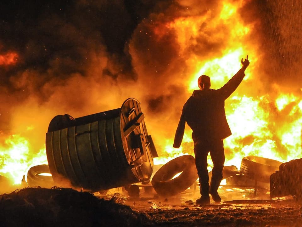 Demonstrant vor einer brennenden Barrikade, die Flammen schlagen meterhoch.