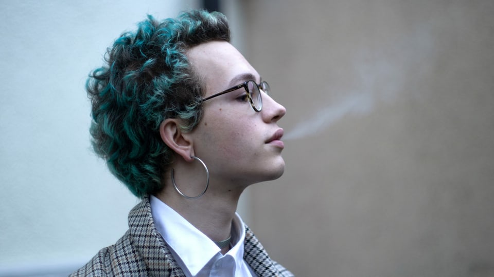 Junger Mann bläst Rauch aus mit grünen Haaren, Ohrringen