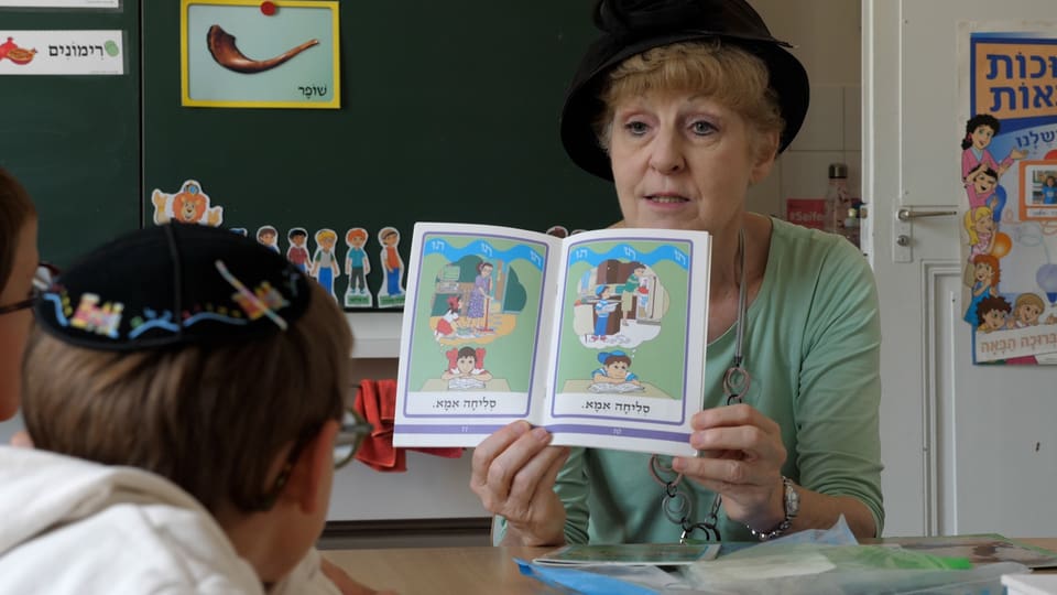Eine Lehrkraft zeigt einem Schüler ein hebräisches Bilderbuch