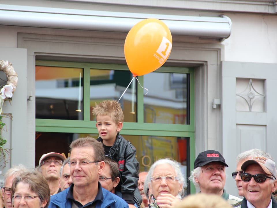 Publikum - Kind sitzt auf den Schultern seines Vaters und hält einen Ballon in der Hand.