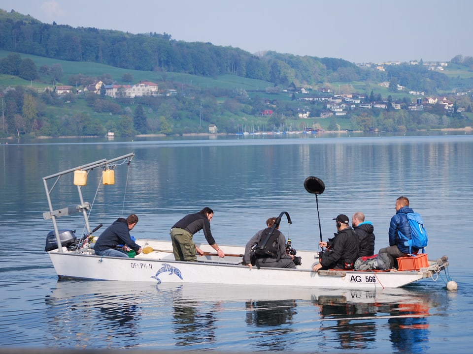 Ein Fischerboot auf dem See. Drin sitzen Nik Hartmann, Fischer Patrick Truttman und 4 Personen des TV-Teams. 