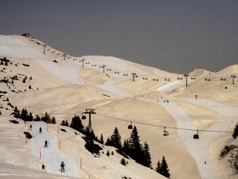 Skigebiet mit Pisten. Der Schnee ist mit Saharastaub gelb verfärbt. Präparierte Pisten und Wege sind weisser. 