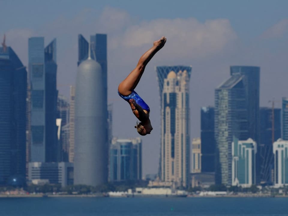 Eine Frau scheint über der Stadt Doha zu fliegen, während dem sie von einem Turm springt.