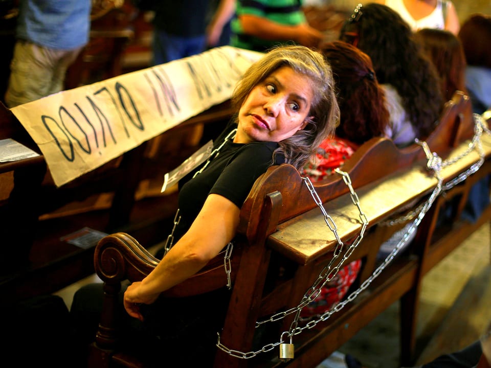 Eine Opfer-Angehörige des Pinochet-Regimes ist an eine Kirchenbank in Santiago, Chile, gekettet. Sie schaut über die Schulter zurück.