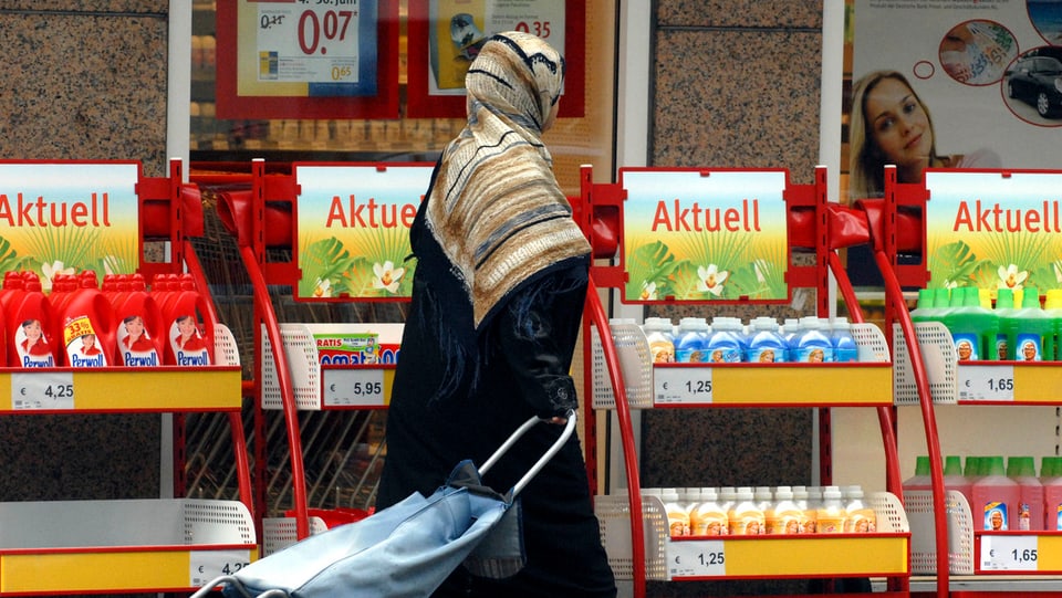 Eine Passantin mit einem Kopftuch geht an einem Einkaufsladen vorbei