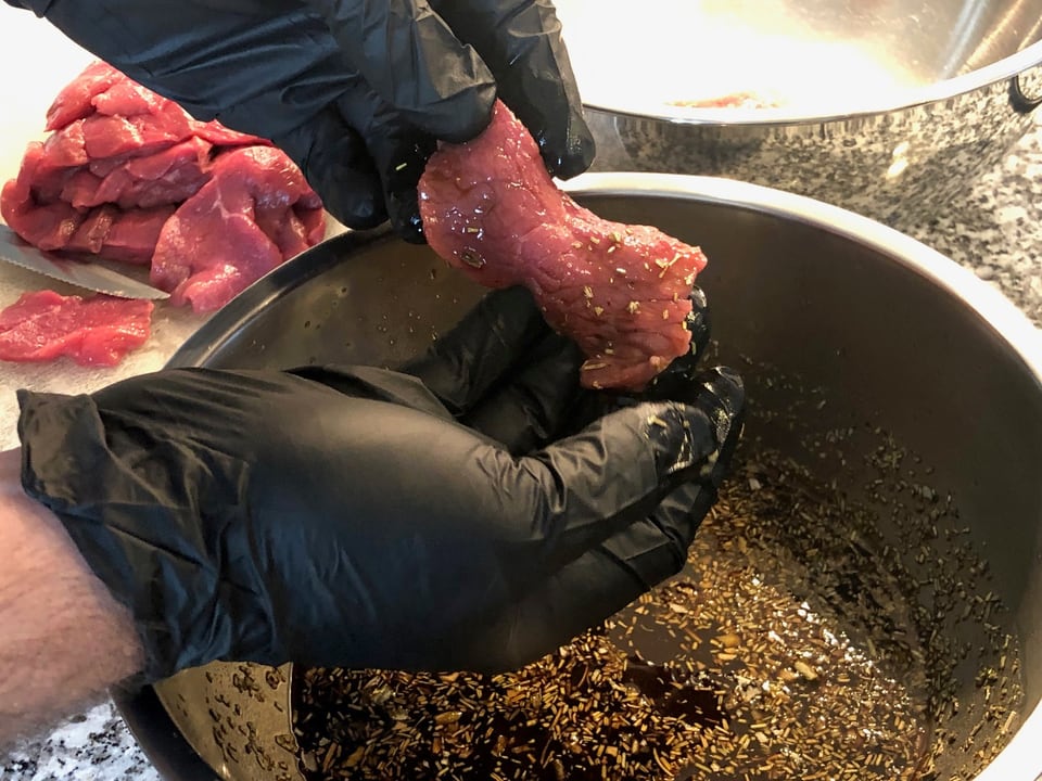 Kleine Rindfleischstücke wird mit der Hand durch die Marinade gezogen. 