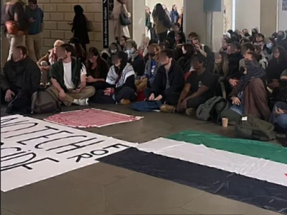 Menschen sitzen auf dem Boden während einer Demonstration in einer Bahnhofshalle.