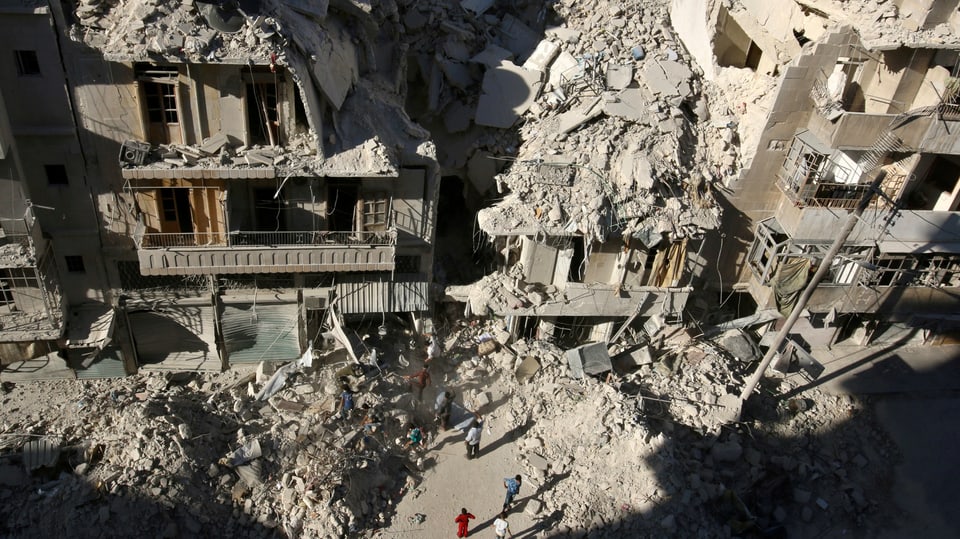 Stark zerstörte Häuser in einer Strasse von Aleppo von oben fotografiert, auf der Strasse Trümmer und Menschen.