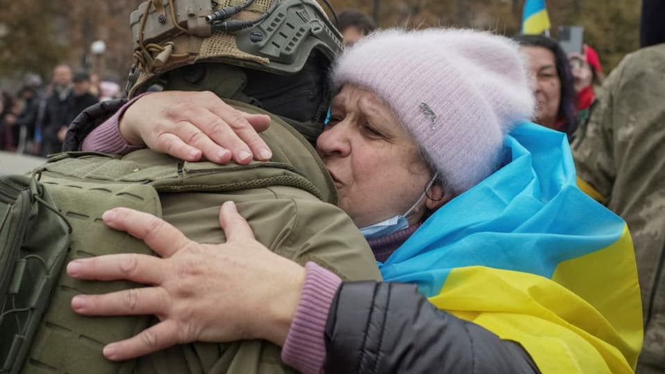 Eine Frau, die eine Ukraine-Flagge auf ihrem Rücken trägt, umarmt einen Soldaten.