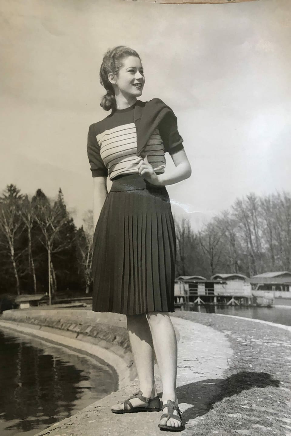 Junge Frau posiert an Seeufer in adrettem Streifenkleid.