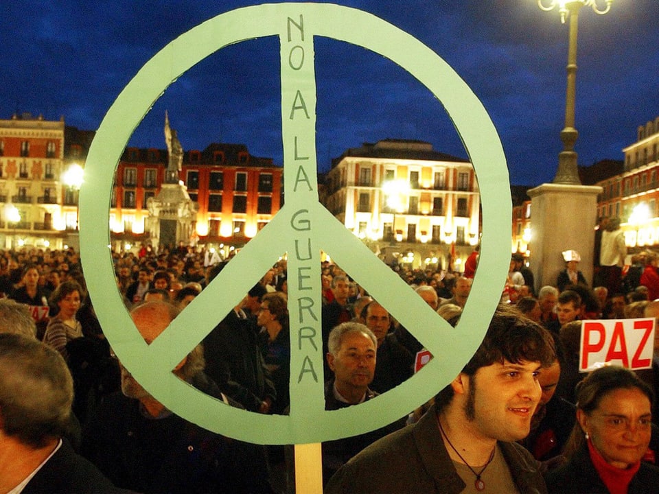 Ein grosses grünes Peace-Zeichen vor einer Menschenmenge auf einem Platz.