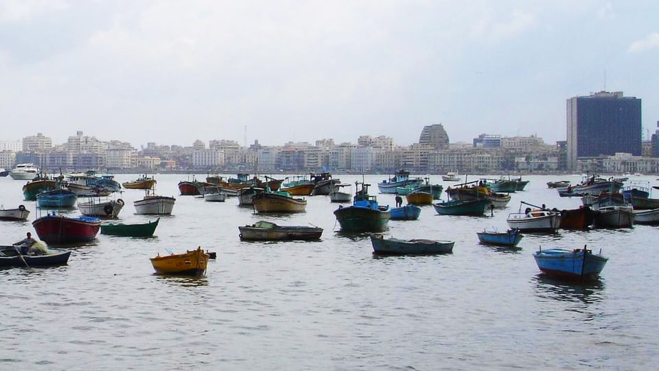 Blick vom Meer auf die Stadt, im Wasser sind zahlreiche kleine Boote.