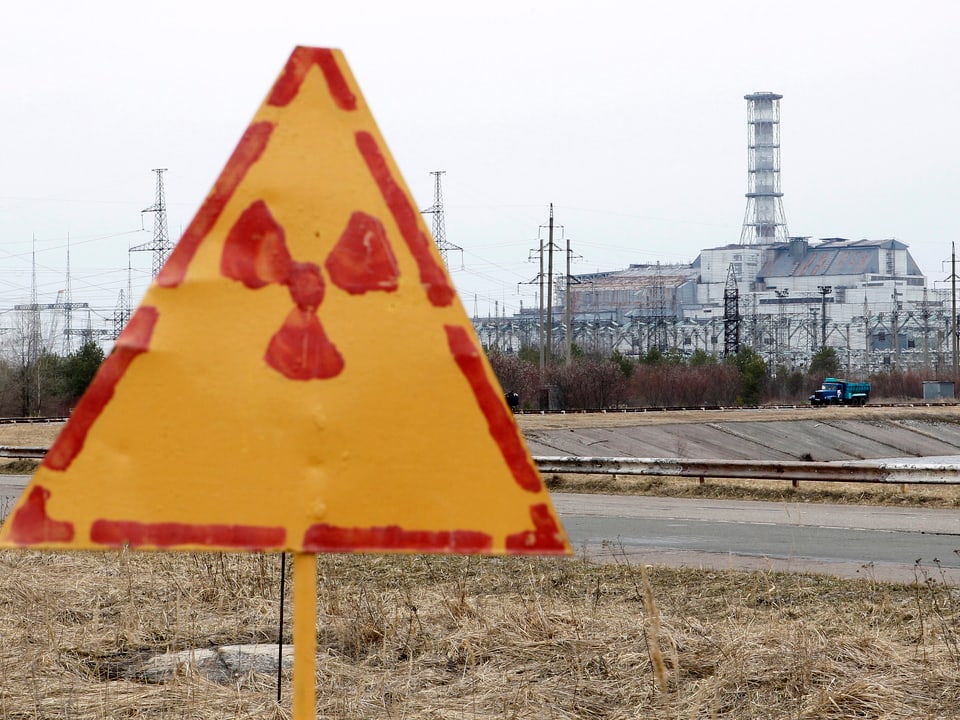 Schild mit Atom-Zeichen vor dem zerstörten Reaktor in Tschenrnobyl.