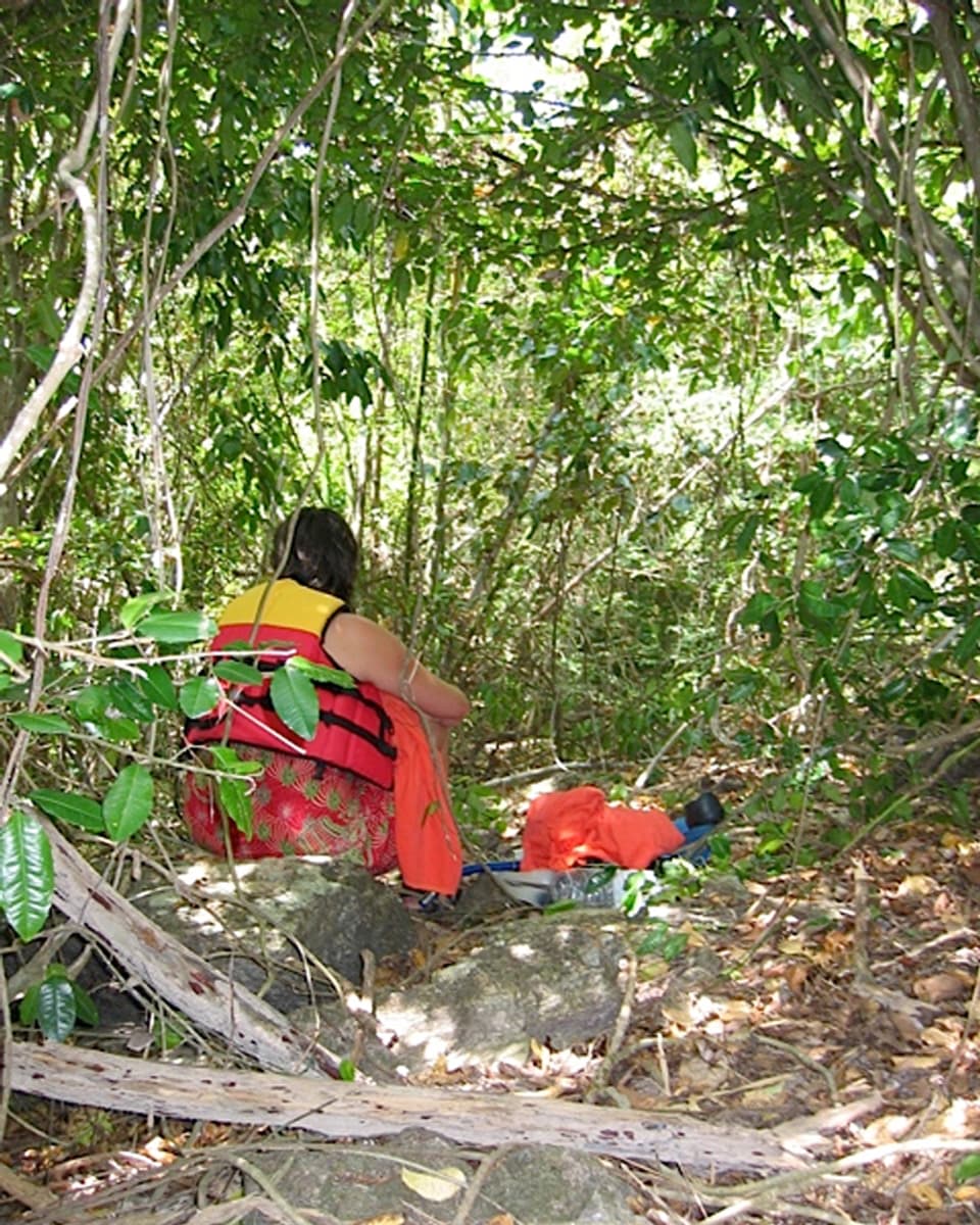 Eine Frau sitzt mit einer Schwimmweste in einem Dschungel.