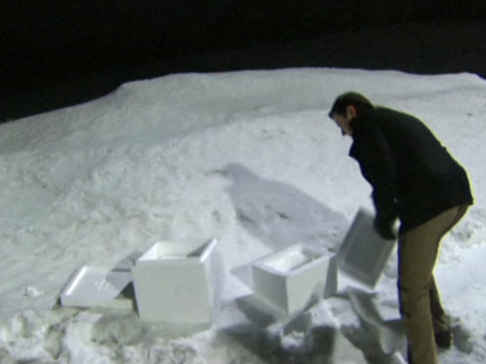 Kyle Waring steht im Schnee und zwei unterschiedlich grossen Paketen voller Schnee.