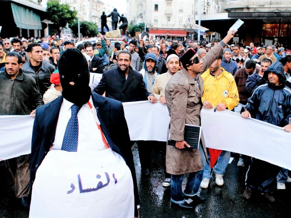 Aktivisten parodieren die marokkanischen Wahlen mit einem maskierten Mann. Auf seinem Bauch steht in arabischer Schrift «Korruption».