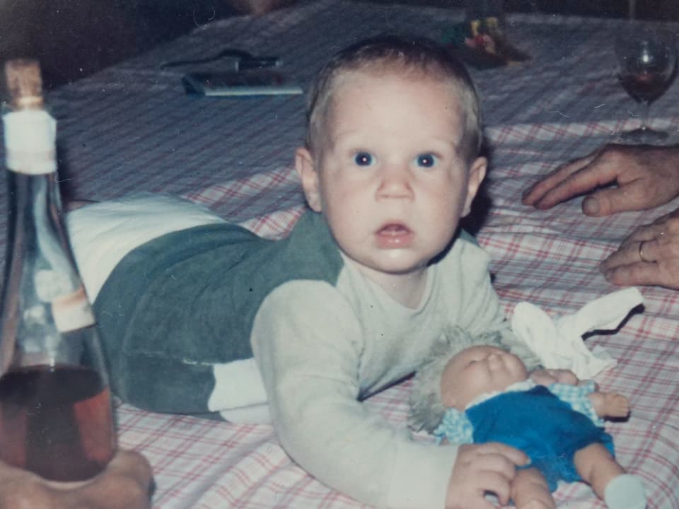 Christian Stucki als Baby auf einer Decke, mit Puppe