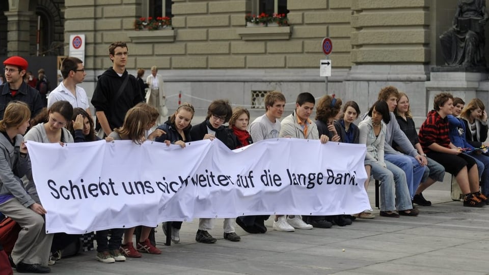 Jugendliche halten ein Transparent in die Höhe. Drauf steht: «Schiebt uns nicht weiter auf die lange Bank».