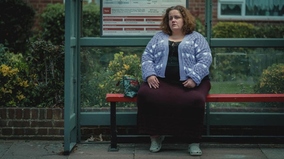 Eine Frau sitzt auf einer Bank in einem Haltestellenhäuschen.