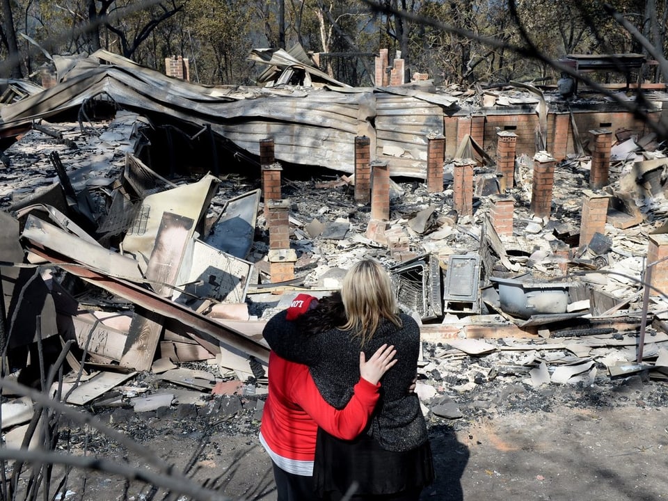 Zwei Personen trauern um ihr abgebranntes Haus.