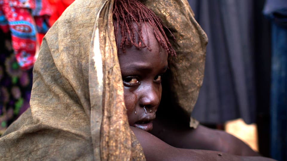 Ein kenianisches Mädchen ist in eine Decke gehüllt und weint.