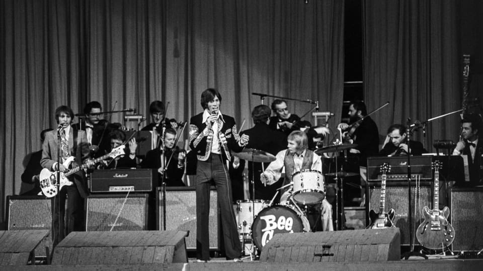 Konzertaufnahme von den Bee Gees, Sänger Barry Gibb hat ein Mikrofon in der Hand.