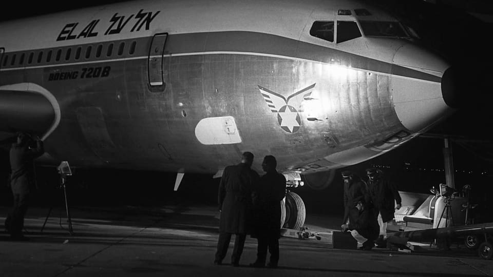 Schwarzweiss-Foto eines Flugzeuges, davor vier Menschen mit dem Rücken zur Kamera.