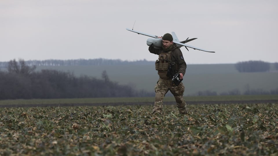 Ein Soldat trägt eine Mehrzweckdrohne Leleka-100 auf einem Feld. 
