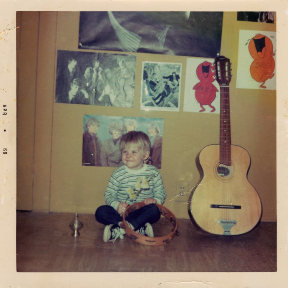 Kurt Cobain als kleiner Junge, neben einer Gitarre sitzend.