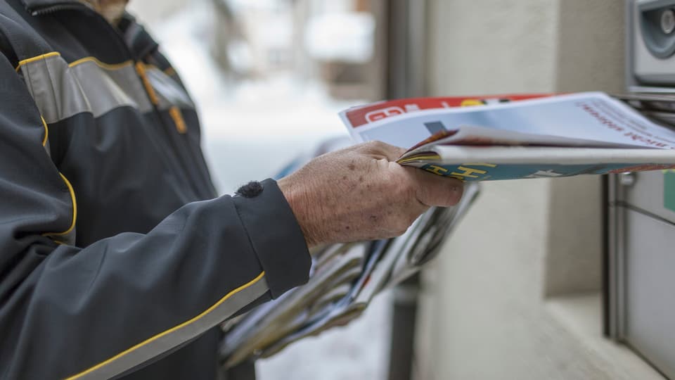 Postbote wirft Zeitschriften in einen Briefkasten.