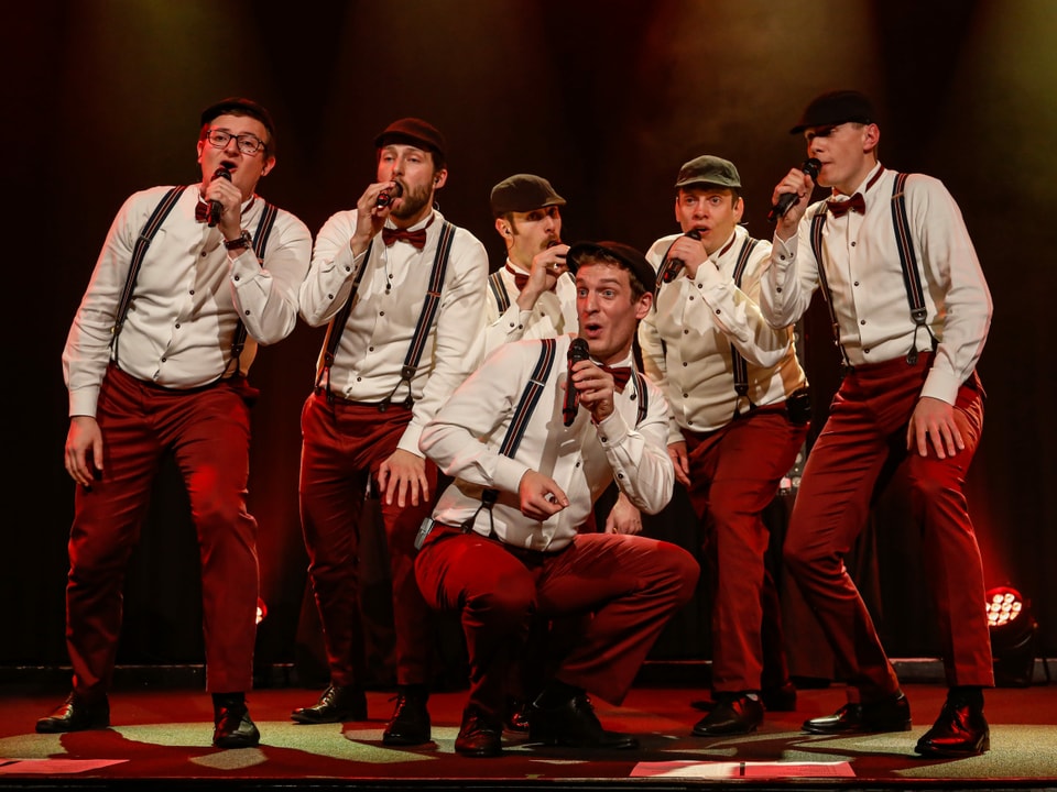 Sechs Männer in denselben Kleidern singen auf der Bühne.