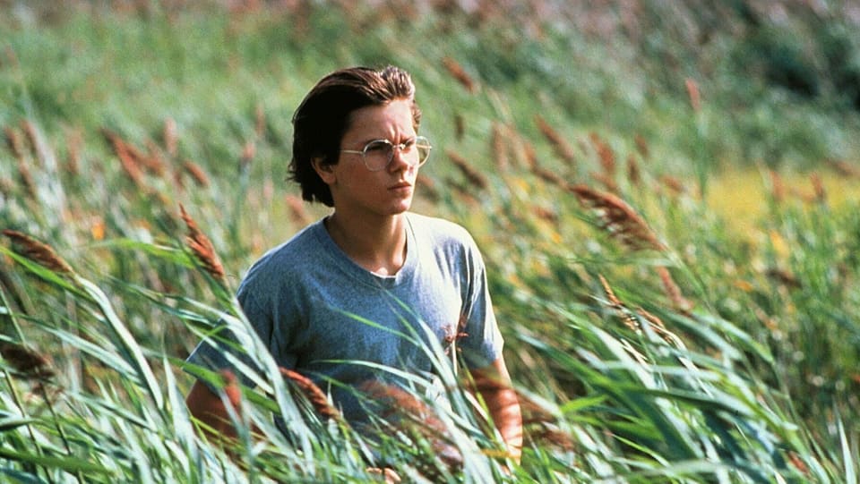 River Phoenix steht für den Film «Running on Empty» mit einer Brille auf der Nase in einem weiten Feld.