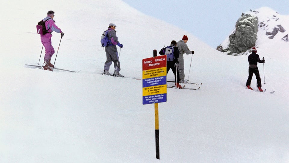Ein Schneehang, im Vordergrund ein Lawinenwarnschild, hinten die Gruppe mit Prinz Charles.