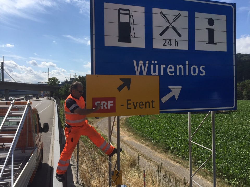 Ein Mann platziert ein Event-Schild auf dem Autobahnschild