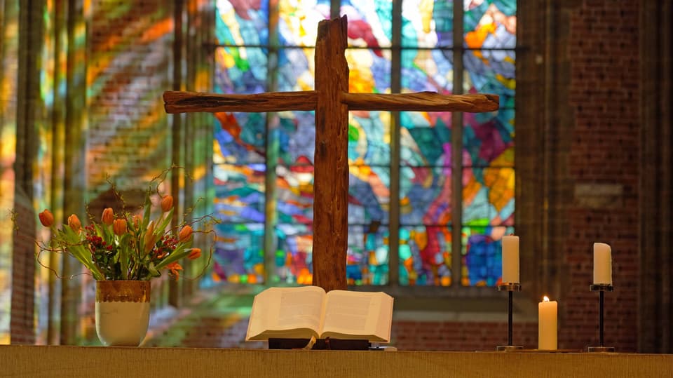 Die Bibel liegt auf dem Altar, daneben Kerzen und Tuplen, dahinter ein Holzkreuz.