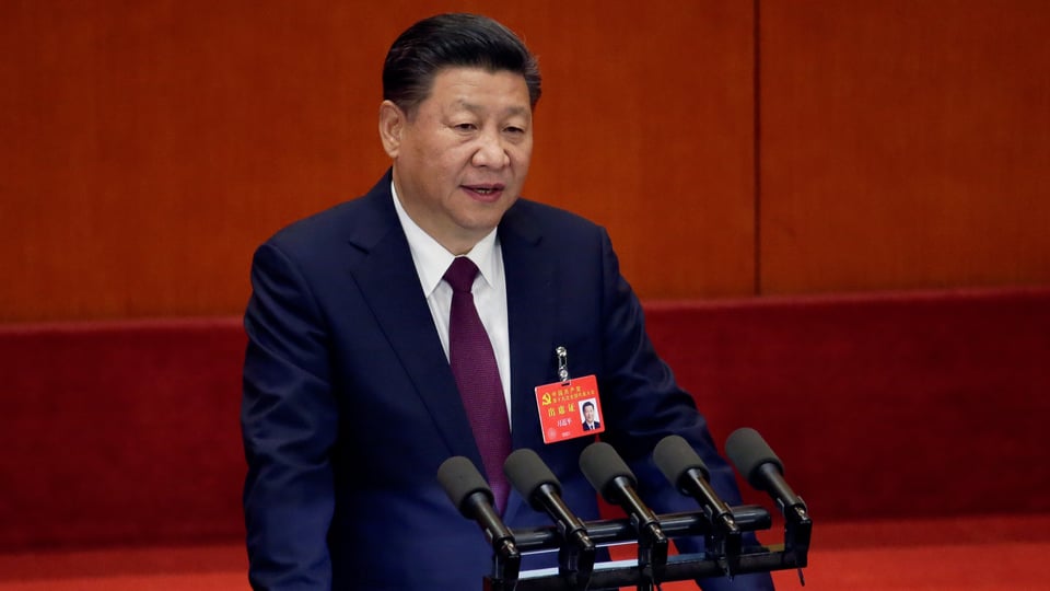 Xi hinter Mikrofonen vor rotem Hintergrund.