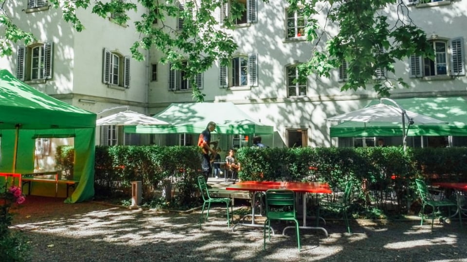 Menschen sitzen auf der Terrasse vor einem grossen Haus